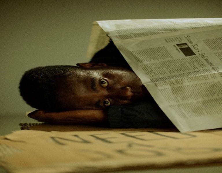 Black-Man-Sleeping-On-His-Sign-on-the-ground-covered-by-a-News-Paper